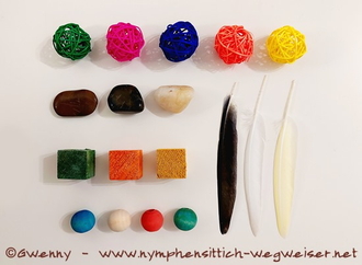 Weidenbälle, Steine, Holzwürfel und -kugeln und Federn in verschiedenen Farben