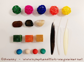 Weidenbälle, Steine, Holzwürfel und -kugeln und Federn in verschiedenen Farben